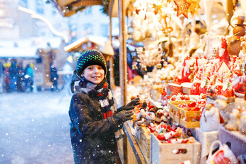 Little cute kid boy selecting decoration on Christmas market. Beautiful child shopping for toys and decorative ornaments stuff for tree. Xmas market in Germany.