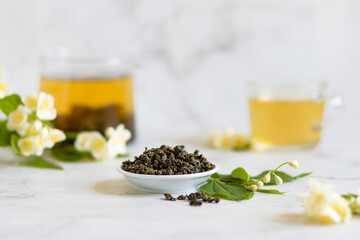 Chinese large leaf green tea with jasmine on white marble background. Dry leaves and brewed herbal drink in teapot and cup