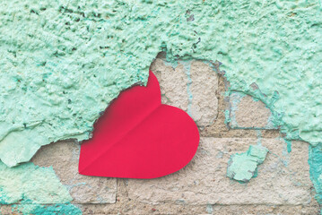 Valentine day background with red paper heart on a rustic green crumbling wall. heart is stuck on...