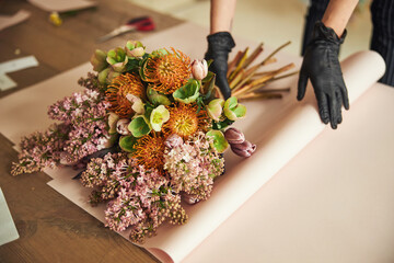 Woman in disposable nitrile gloves wrapping a mixed flower bouquet