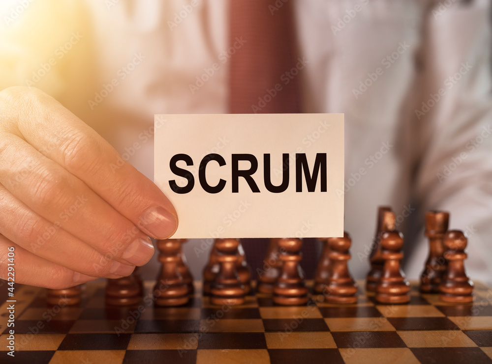 Poster scrum word on paper in businessman hand close up over chessboard. concept of methods in management.