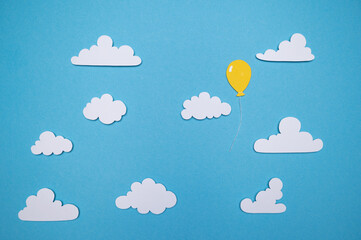 Paper cut out balloons floating through a blue sky and fluffy white clouds