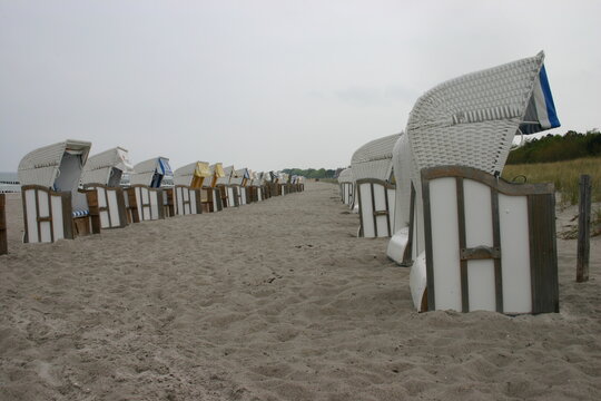 Eine Reihe leerer Strandkörbe unter grauem Himmel