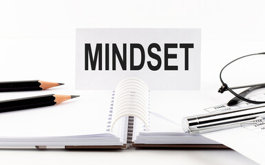 Text MINDSET on paper card,pen, pencils, glasses,financial documentation on table - business concept
