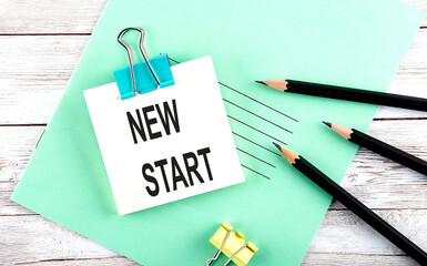 Text NEW START on the short note with pencils on wooden background