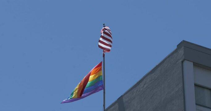 Unites States and gay pride flag blowing together in the wind on top of a building