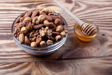 Assorted nuts in glass bowl with honey bowl and honey dipper. Mixed nuts on wooden table. Black stone plate on wooden background.