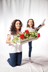 Daughter and mother with flowers in the studio on a white background. Teenager girl and woman posing indoors. Family during photo shoot in summer or spring time