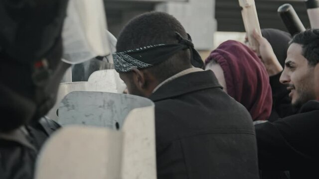 Handheld slowmo shot of young protesters pushing against riot police shields