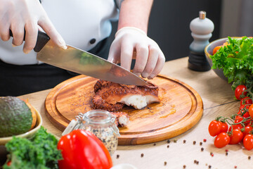 Young chef is cutting octopus in a modern kitchen. The man prepares food at home. Cooking healthy and tasty food.