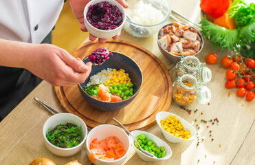 Young prepares a poke bowl in a modern kitchen. The man prepares food at home. Cooking healthy and...