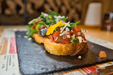 Vorspeise, Bruschetta mit Blüte und Wildkräuter auf einem schwarzen Steinteller