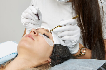 Master in a protective mask for eyelash extension uses tweezers to fix the eyelashes. Close-up of a cosmetic procedure for the design of the look