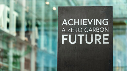 Achieving a zero-carbon future  on a city-center sign in front of a modern office building	
