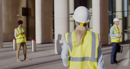 Back view of female engineer in safety hardhat and vest entering office building