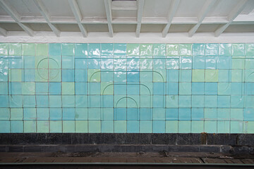 Old track wall at the metro station, lined with shabby turquoise glazed ceramic tiles.