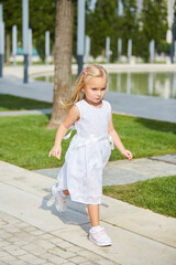 Fototapeta premium A little blonde girl in a white dress walks in the Park.