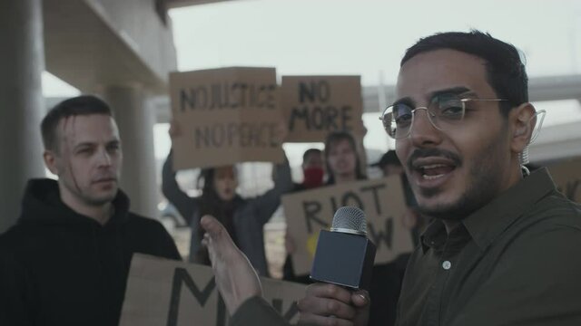 Slowmo shot of TV reporter talking to camera and interviewing wounded young man with sign at protest