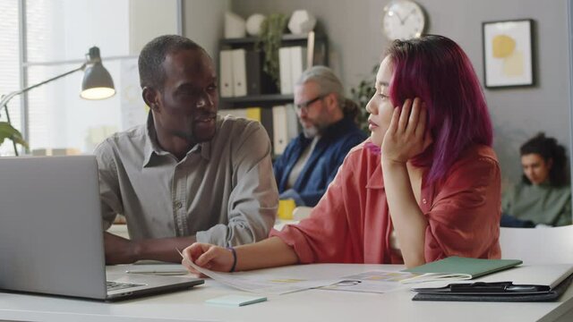Afro-American male manager speaking with young Asian female trainee while working together in office