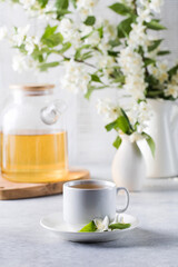 A mug of green tea with jasmine on the background of a teapot of tea and a branch of jasmine.