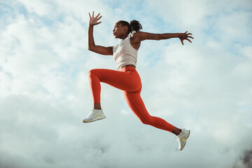 Woman running and jumping in midair against sky