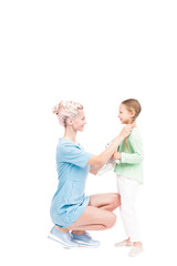 Vertical full length isolated shot of modern mother sitting in front of her daughter fixing her hair, white background