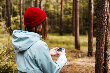 A women in red hat and blue coat holds a compass in hand and is guided by the area, autumn forest, walk,hiking