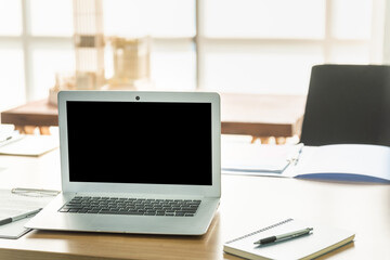 Closeup of notebook computer laptop black blank screen copy space on wooden work desk with book, clipboard and pen in office.