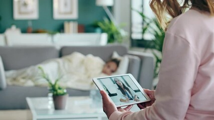 Video of mature mother making videocall with young female doctor while caring for her sick daughter in living room at home.