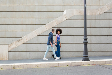 young couple Caucasian man and African American woman holding hands around city with blue casual clothes and a gray wall