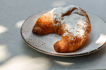 Fresh baked butter croissant with sugar powder on light vintage ceramic plate closeup. Light and shadow