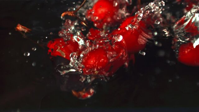 Super slow motion cherry falls into the water with splashes and air bubbles. On a black background.Filmed on a high-speed camera at 1000 fps.