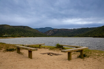 Obraz premium Four wooden benches on a beach with water and hills in the back ground.