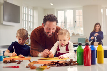 Father With Children At Home Doing Craft And Making Picture From Leaves In Kitchen