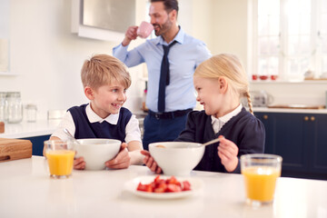 Two Children Wearing School Uniform In Kitchen Eating Breakfast As Father Gets Ready For Work