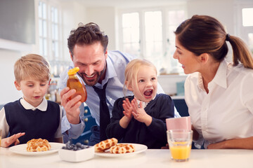 Obraz na płótnie Canvas Children Wearing School Uniform In Kitchen Eating Breakfast Waffles As Parents Get Ready For Work