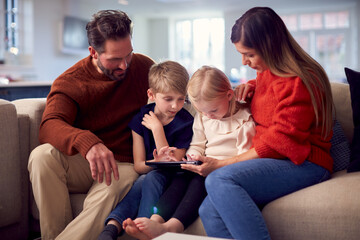 Family Sitting On Sofa Watching Digital Tablet Together