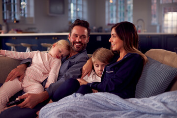 Family In Pyjamas Sitting On Sofa Watching TV Together As Children Fall Asleep