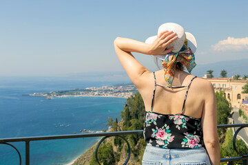 Beautiful woman with hat enjoying view of Etna volcano and Ionian sea from stunning village of...