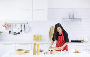 Content Asian woman in apron standing at table with assorted ingredients and preparing tasty food in kitchen at home