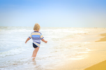 Fototapeta premium Toddler blonde child running on the beach. Copy space. Sunset summer background. 