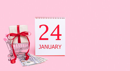 A gift box in a shopping trolley, dollars and a calendar with the date of 24 january on a pink background.