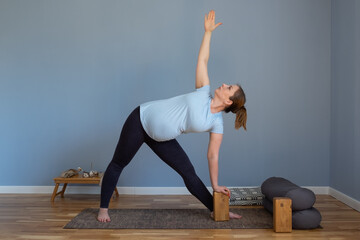 Naklejka premium Pregnant yoga model working out indoo doing Extended Triangle pose