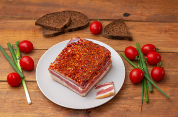 Smoked spicy bacon on a plate. Slice of smoked pork meat on bread, cherry tomatoes and green onion on wooden table.