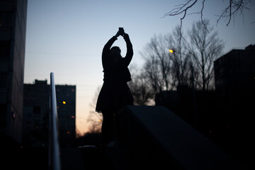 The silhouette of a girl taking a photo of the evening sky.
