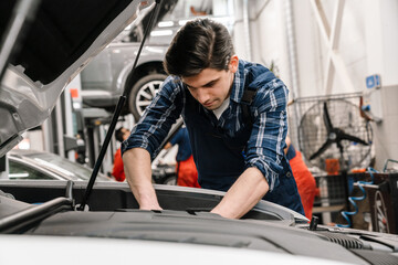 Young car mechanic fixing car while working in garage indoors