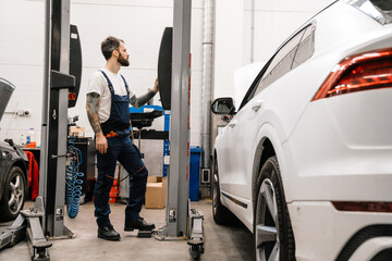 Bearded car mechanic testing car while working in garage indoors