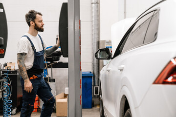 Obraz na płótnie Canvas Bearded car mechanic testing car while working in garage indoors