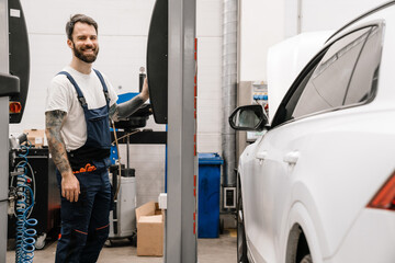 Fototapeta na wymiar Bearded smiling car mechanic testing car while working in garage