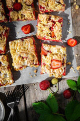Strawberry and rhubarb meringue crumble squares on baking paper on old wooden table.